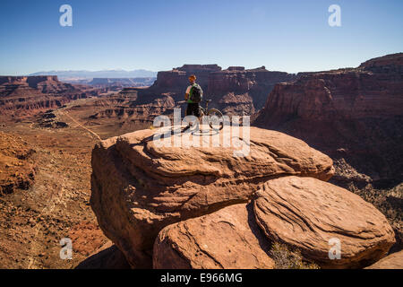 Whit Richardson stehen mit seinem Mountainbike mit Blick auf Shafer Canyon auf dem White Rim Trail, Canyonlands National Park, Moab, Stockfoto