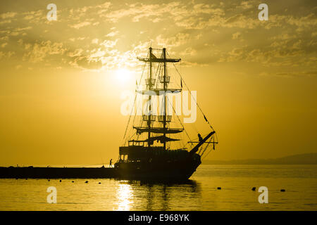 Sonnenuntergang über dem Meer und ein einsamer Segelschiff in der Bucht. Stockfoto