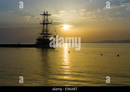 Sonnenuntergang über dem Meer und ein einsamer Segelschiff in der Bucht. Stockfoto