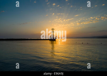 Sonnenuntergang über dem Meer und ein einsamer Segelschiff in der Bucht. Stockfoto