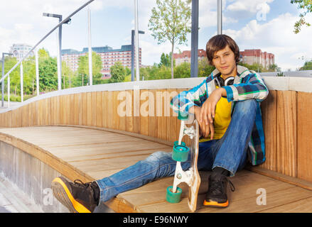 Junge hält Skateboard während sitzt mit Arm am Knie Stockfoto