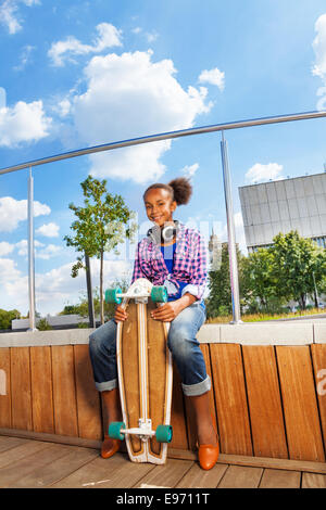 Afrikanische Mädchen hält Skateboard und sitzen auf Seite Stockfoto