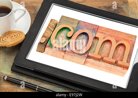 Dot Com kommerzielle Internetdomäne im Buchdruck Holzart Druckstöcken auf einem digitalen Tablet-Bildschirm mit einer Tasse Kaffee Stockfoto