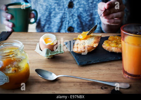 Frühstück mit weich gekochtes Ei, Orangen-Saft, toast mit Marmelade und Kaffee mit Milch auf einem Holztisch. Stockfoto