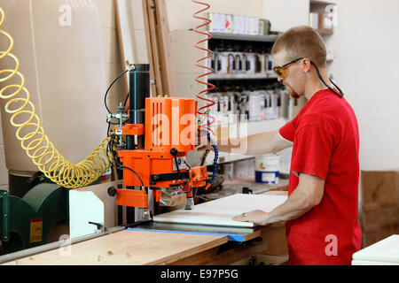 Ein Zimmermann, der mit einer Bohrmaschine die Einschublöcher in die Seite eines Schranks bohrt. Stockfoto