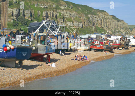 Menschen am Hastings Stade Strand direkt am Strand Sonnenbaden startete Flotte Fischtrawler, East Sussex, England, UK, GB Stockfoto