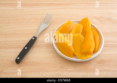 Eine Platte aus der Dose Mango Scheiben auf einer hölzernen Tischplatte mit einer Gabel zur Seite. Stockfoto