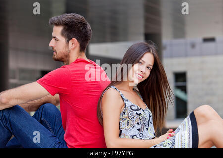 Glückliches junges Paar sitzt Rücken an Rücken auf dem campus Stockfoto