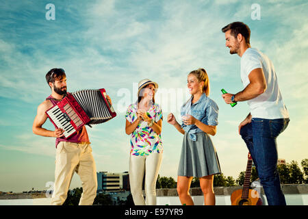 Man spielt Akkordeon während Freunde tanzen Party auf dem Dach Stockfoto