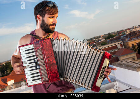 Junger Mann spielt Akkordeon auf Dachterrasse Stockfoto