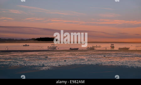 Blick auf den Sonnenuntergang Orange, Blues und Purpur, von einem Strand mit Sportboote vor Anker bei Ebbe. Himmel spiegelt sich in dem nassen Strand. Stockfoto