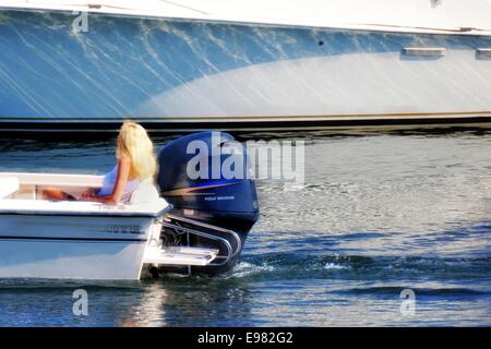 Blonde Frauen sitzen auf der Rückseite Motorboot neben großen blauen Außenbordmotor. Ihr Boot ist viel größeren weißen Yacht vorbei Seite bewegen. Stockfoto