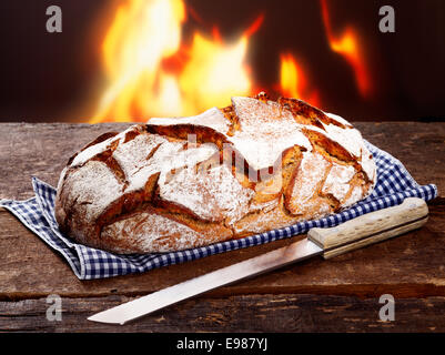 Knackige Laib frisch gebackenes Roggenbrot mit einem Messer auf ein aufgegebenes Serviette vor einem lodernden Feuer Stockfoto