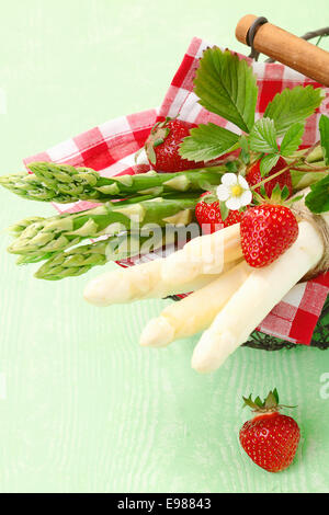 Portion frische grünen und weißen Spargelspitzen auf einer fröhlichen roten und weißen aufgegebenes Serviette mit Erdbeeren Stockfoto