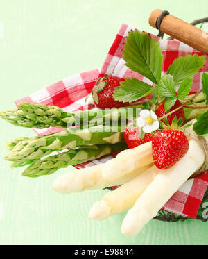 Portion frische grünen und weißen Spargelspitzen auf einer fröhlichen roten und weißen aufgegebenes Serviette mit Erdbeeren Stockfoto