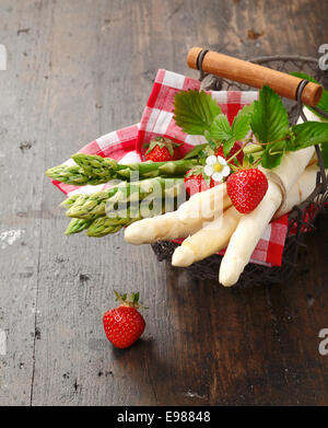 Grünen und weißen Spargel und Erdbeeren in einen Drahtkorb auf hölzernen Hintergrund Stockfoto