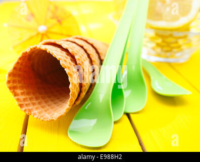 Nahaufnahme von einem Stapel von vier leere Wafer Icecream Zuckertüten mit grünem Plastik Löffel auf einer hölzernen Tischplatte gelb Stockfoto