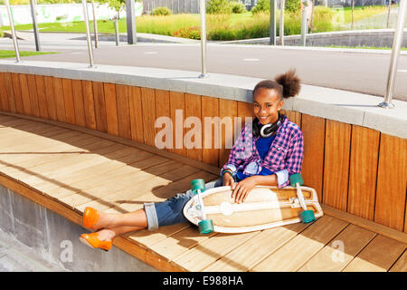 Afrikanische Mädchen sitzen und halten skateboard Stockfoto