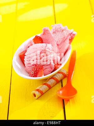 Erdbeer Eis mit gewürfelten reifen roten frischen Früchten serviert auf einem gelben Tisch mit einem dekorativen gestreiften Wafer-biscuit Stockfoto