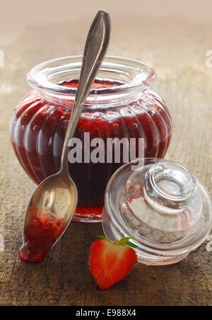 Köstliche hausgemachte Erdbeermarmelade in einem dekorativen Glas mit einem Teelöffel Marmelade auf die hölzernen Tischplatte ruht auf der Felge dribbling geriffelt Stockfoto