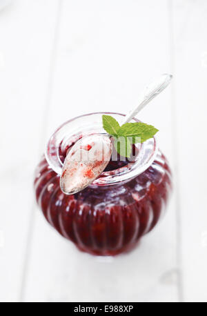 Elegante geriffeltes Glas Beeren Marmelade mit einem gebrauchten Silber Teelöffel Marmelade ruht auf der Felge mit drei frische Minze ummantelt Stockfoto