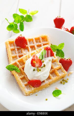 Knusprige goldene Waffeln, Erdbeeren und Sahne garniert mit frischer Minze und bestreut mit Zucker für eine köstliche Sommer-dessert Stockfoto