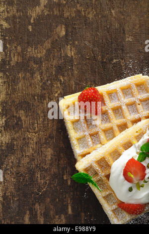 Draufsicht der goldene Waffeln mit Sahne und Erdbeeren auf einem grob strukturierten Holztisch mit Exemplar Stockfoto