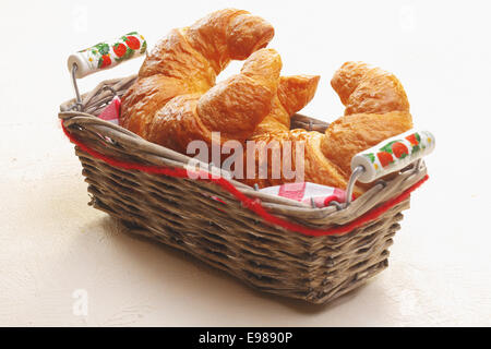 Korb mit frisch gebackenen goldenen Halbmond-förmige Croissants auf einer weißen Tischplatte, als Beilage zu einer Mahlzeit zu dienen Stockfoto