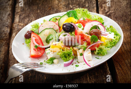 Portion Frische gesunde gemischter Salat mit Blattgemüse, Rettich, Tomaten, Oliven und Käse auf einem rustikalen Holztisch serviert Stockfoto