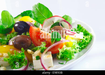 Detailansicht einer Portion knackige appetitlich griechischer Salat mit Kopfsalat, Basilikum, Schafskäse, Zwiebeln, Oliven, Radieschen und Tomaten Stockfoto