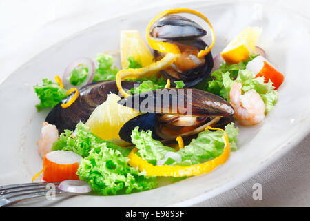 Servieren köstliche Meeresfrüchte Salat mit Muscheln, Krabben und Garnelen auf einem Bett aus knackigen grünen Salat garniert mit Orangenschale Stockfoto