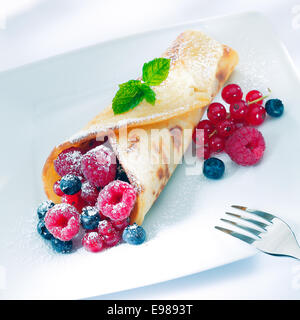 Beeren-Pfannkuchen mit Zucker mit einem Sortiment oder reife Himbeeren, Johannisbeeren und Heidelbeeren garniert mit Minze bestreut Stockfoto