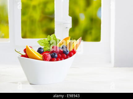 Bunte Schale mit tropischen Früchten mit einem Sortiment von Himbeeren, Heidelbeeren, Johannisbeeren und in Scheiben geschnittenen Orangen garniert mit frischer Minze mit Exemplar Stockfoto