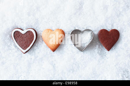 Romantische Weihnachten Herzkekse mit Lebkuchen und einem herzförmigen Metall Ausstecher in einer Linie im Neuschnee mit Exemplar Stockfoto