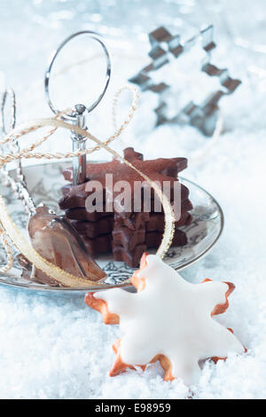 Leckerste frisch gebackene Sterne Weihnachtsplätzchen mit weiß und Schoko-Glasur serviert auf einem Teller im Schnee mit einer dekorativen Schleife Stockfoto