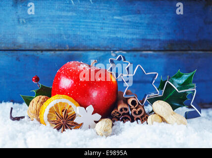 Bunte Weihnachten Stillleben Hintergrund Witz ein reifer roter Apfel, Gewürzen, Nüssen und Metall Sterne eingebettet in Schnee vor blauen Holztafeln mit Exemplar Stockfoto