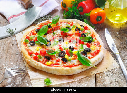 Frisch zubereitete vegetarische Pizza serviert auf Papier Backofen in der Küche umgeben von verschiedenen Zutaten bei der Zubereitung verwendet Stockfoto