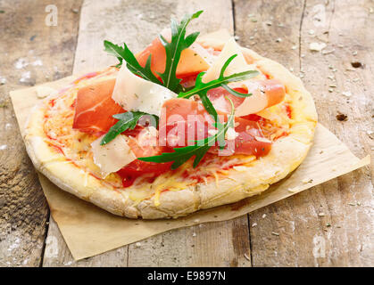 Frisch zubereitete leckere Pizza auf dem Ofen Papier mit einem goldenen Sockel mit leckeren Schinken, Käse, Tomaten und frischen grünen Kräutern garniert Stockfoto