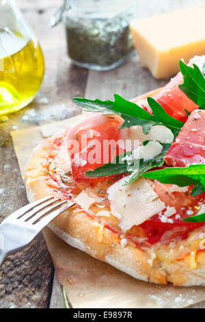 Nahaufnahme von eine köstliche italienische Pizza mit Rucola, Parmesankäse und Parmaschinken auf einem dicken knusprig goldene Sockel auf einem hölzernen Hintergrund Stockfoto