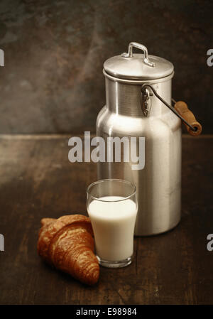 Gesunde frischer Milch zum Frühstück in einen hohen Becher frisch aus der Metall Milch verzichtet und kann mit einem knackigen goldenen Croissant in einer rustikalen Küche serviert Stockfoto