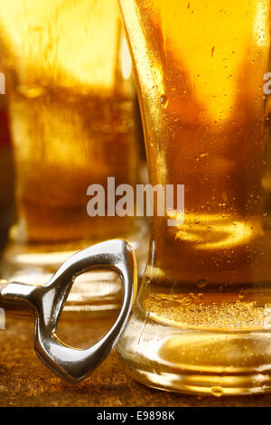 Flaschenöffner auf eine hölzerne Tischplatte gelehnt ein großes Glas voll mit gekühlten goldene Bier, beschnitten Closeup Bild Stockfoto