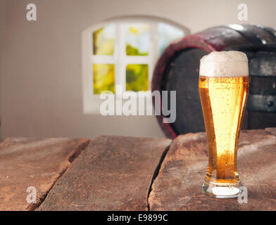 Elegantes Glas helles Bier oder Bier stehend auf einem alten Holztisch vor ein Vintage Eiche Fass in das Innere eines Restaurant oder Pub mit Exemplar Stockfoto