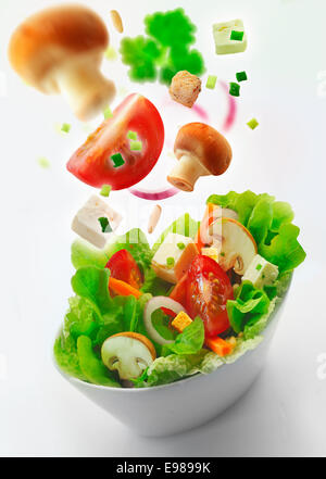 Einzelne Seite Schüssel mit gesunder frischer gemischter Salat von Salat, Karotten, Zwiebel, Champignons, Tomaten und Feta mit weiteren Zutaten in th Luft zurück in die Ferne auf weißem Hintergrund Stockfoto