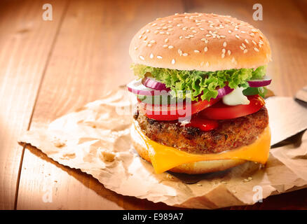 Köstliche Cheeseburger Stapeln mit einem saftigen Rindfleisch Patty, Käse, frischem Salat, Zwiebeln und Tomaten auf einem frischen Brötchen mit Sesam Stockfoto