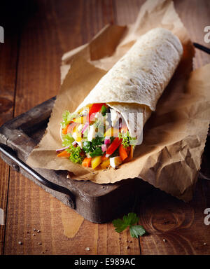 Gerollte goldenen Pfannkuchen gefüllt mit Feta-Käse und bunten gesunde gewürfelt und in Scheiben geschnittenen frischen Gemüse auf trashigen braunem Papier auf eine alte Pfanne serviert Stockfoto