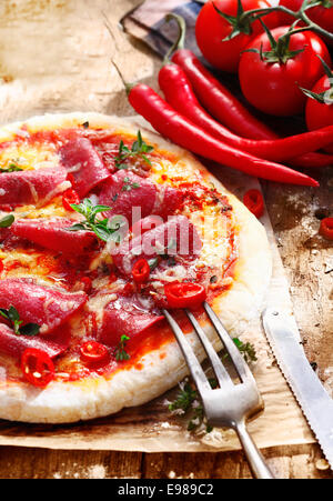 Lecker frisch hausgemacht-Peperoni-Pizza serviert mit in Scheiben geschnittenen heiße rote Chilischote auf eine Grunge Ofen Papier Stockfoto