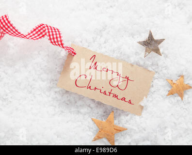 Geschenkanhänger mit Frohe Weihnachten Gruß und eine rote und weiße aufgegebenes Zierband auf einem Bett aus Winter Schnee mit Sternen Stockfoto
