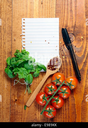 Seite der weißen leeren Liniertes Papier zerrissen von einem Ringbound Notebook auf einem Holztisch mit frischen Kräutern, Tomaten und Pfefferkörner in einem Holzlöffel mit einem Stift schreiben Ihr Rezept, Menü oder Lebensmittelgeschäft Liste Stockfoto