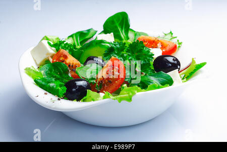 Portion frischer griechischer Salat mit Blattgemüse, Kräuter, Tomaten, Feta und Oliven auf weißem Hintergrund Stockfoto