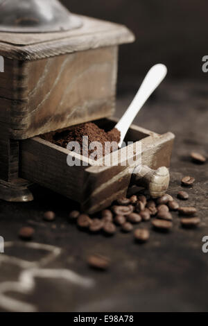 Haufen von frisch gemahlenem Kaffee Körner in die geöffnete Schublade eine alte rustikale Holz Kaffeemühle mit einem Messlöffel in einer Landhausküche Stockfoto